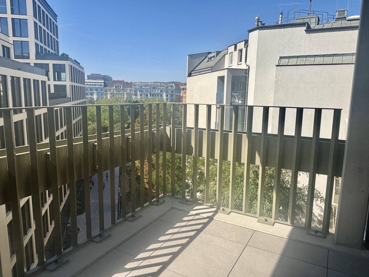 Heller Balkon mit modernem Geländer und Blick auf die umliegenden Gebäude und Bäume.