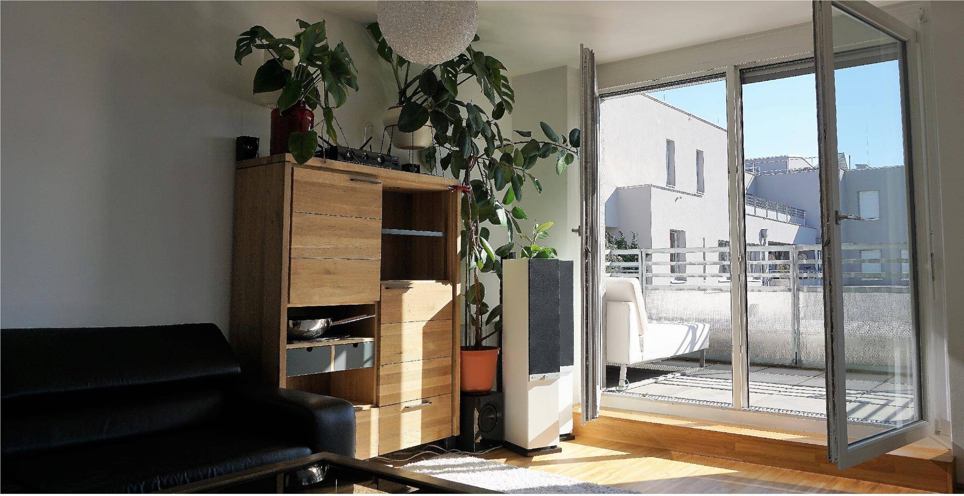 Lichtdurchflutetes Wohnzimmer mit Pflanzen und direktem Zugang zur Terrasse.