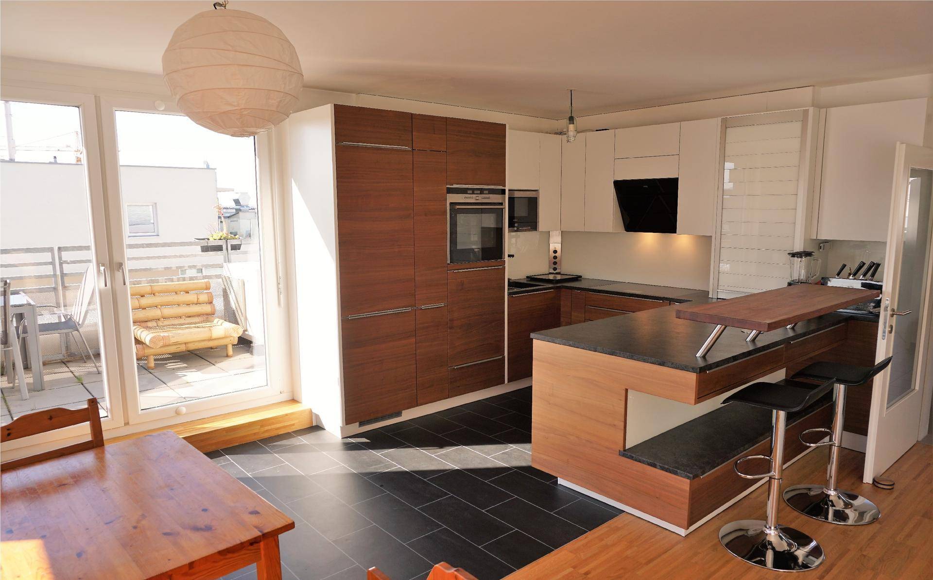 Moderne Einbauküche mit Kochinsel, Barhockern und direktem Zugang zur Terrasse.
