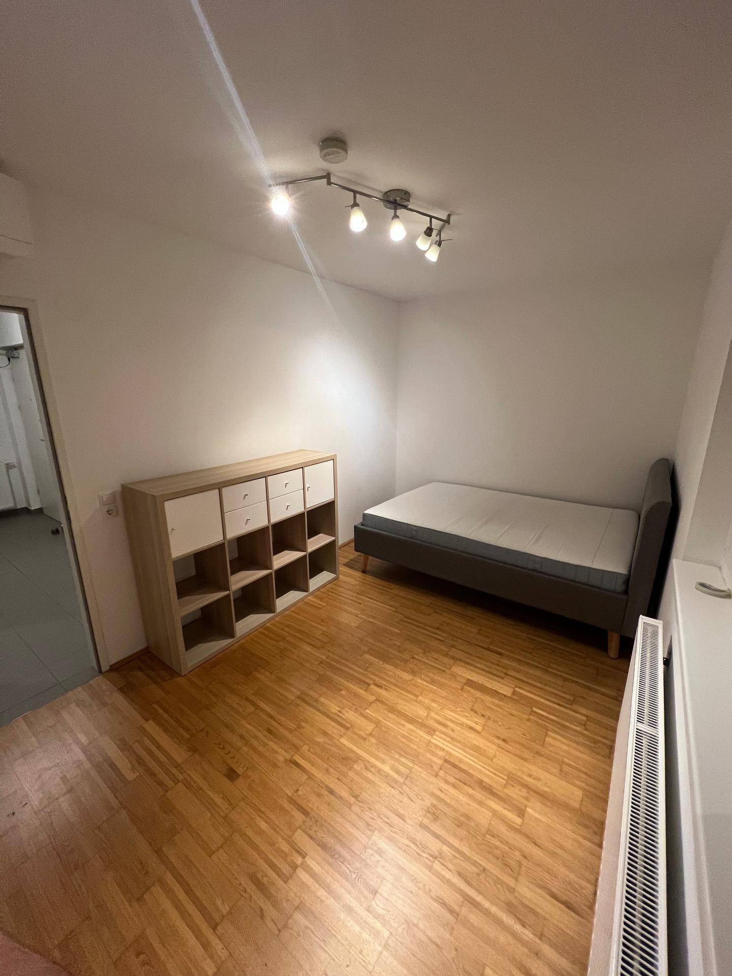 Helles Schlafzimmer mit Parkettboden, Einzelbett und praktischem Regal für Stauraum.