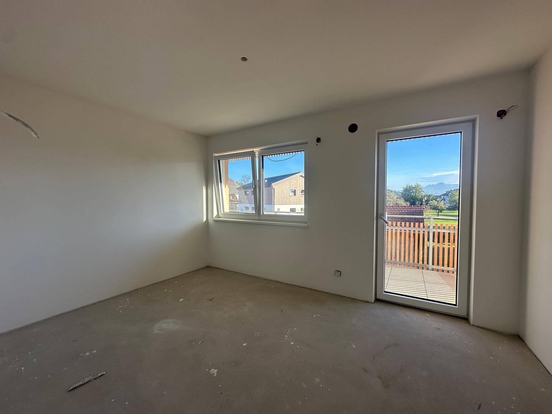 Heller, unmöblierter Raum mit Zugang zu einem Balkon und Blick ins Grüne.