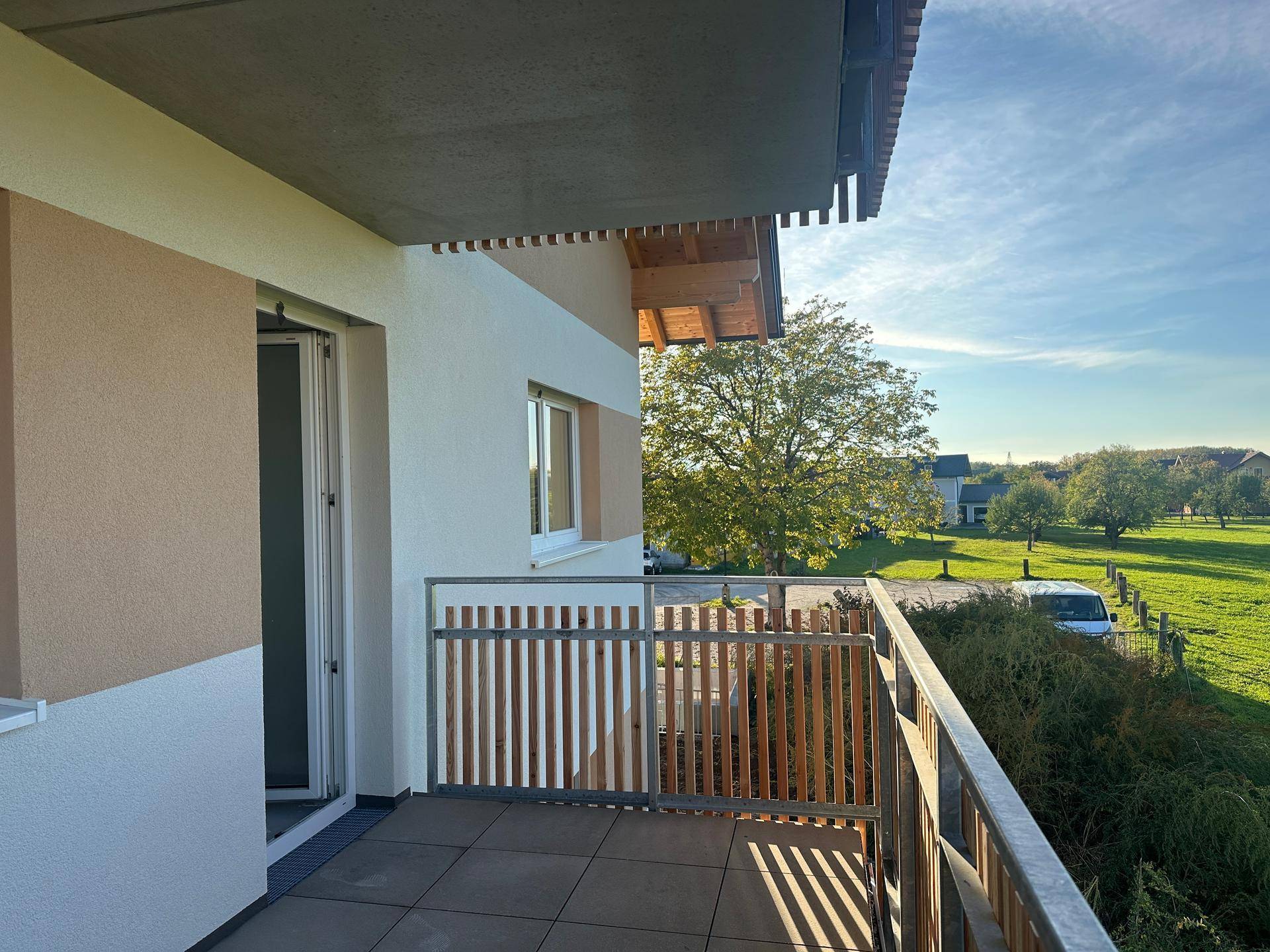 Heller Balkon mit Holzzaun und Zugang zum Innenraum, bietet einen weiten Blick auf die Landschaft.