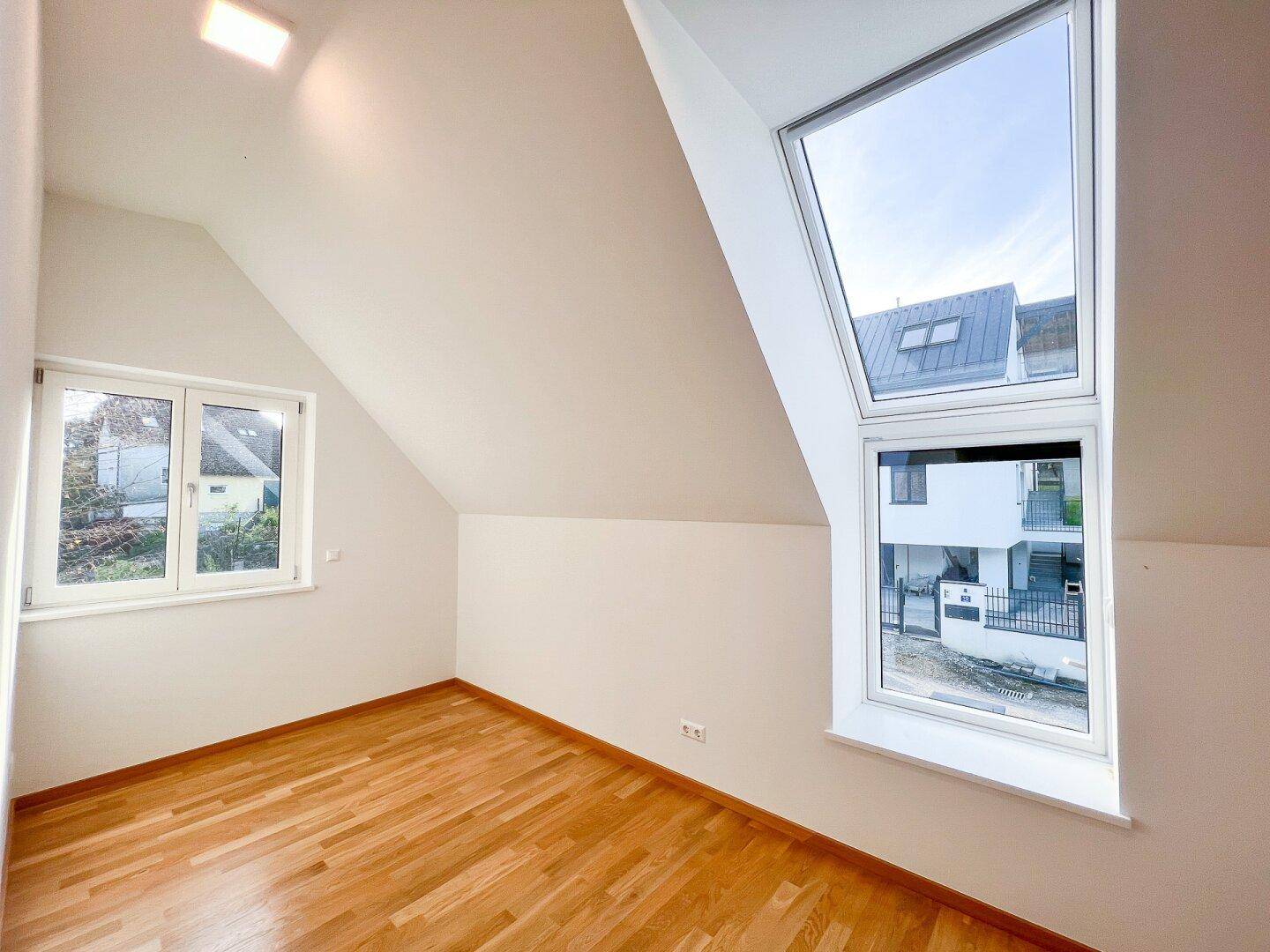 Schlafzimmer mit Dachschrägen, Holzboden und großen Dachfenstern für viel Tageslicht.