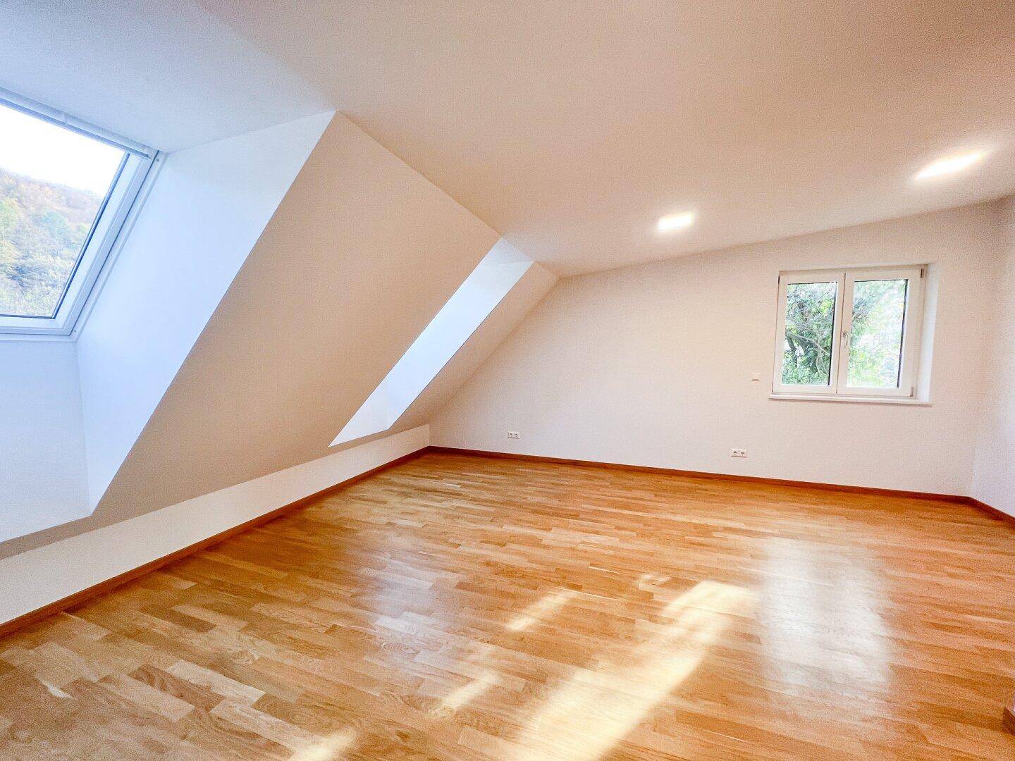Geräumiges Schlafzimmer mit Holzboden und Dachschrägen, bietet eine helle und gemütliche Atmosphäre.
