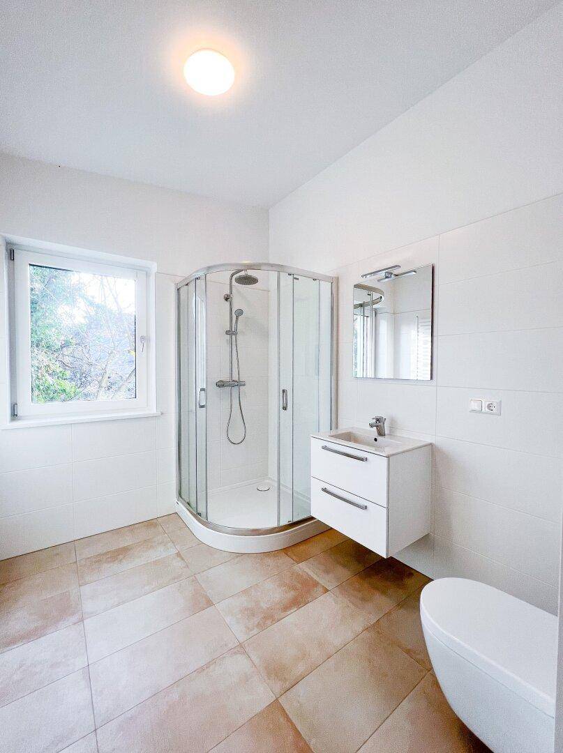 Modernes Badezimmer mit Duschkabine, Waschbecken und Fenster für natürliche Belüftung.