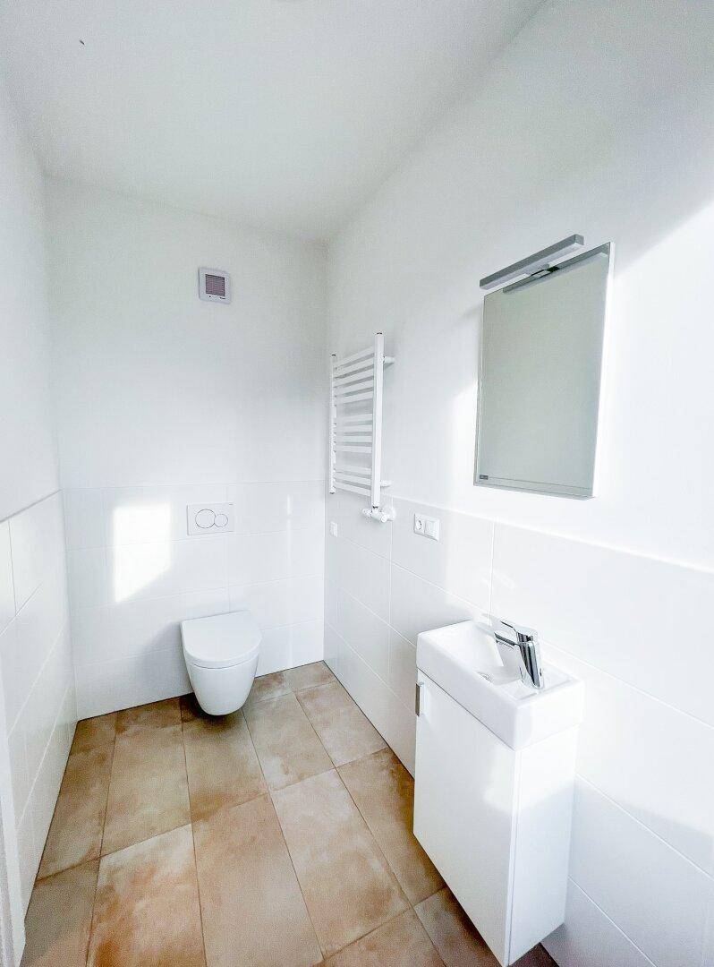 Modernes Gäste-WC mit wandhängender Toilette, kleinem Waschbecken und beheiztem Handtuchhalter.