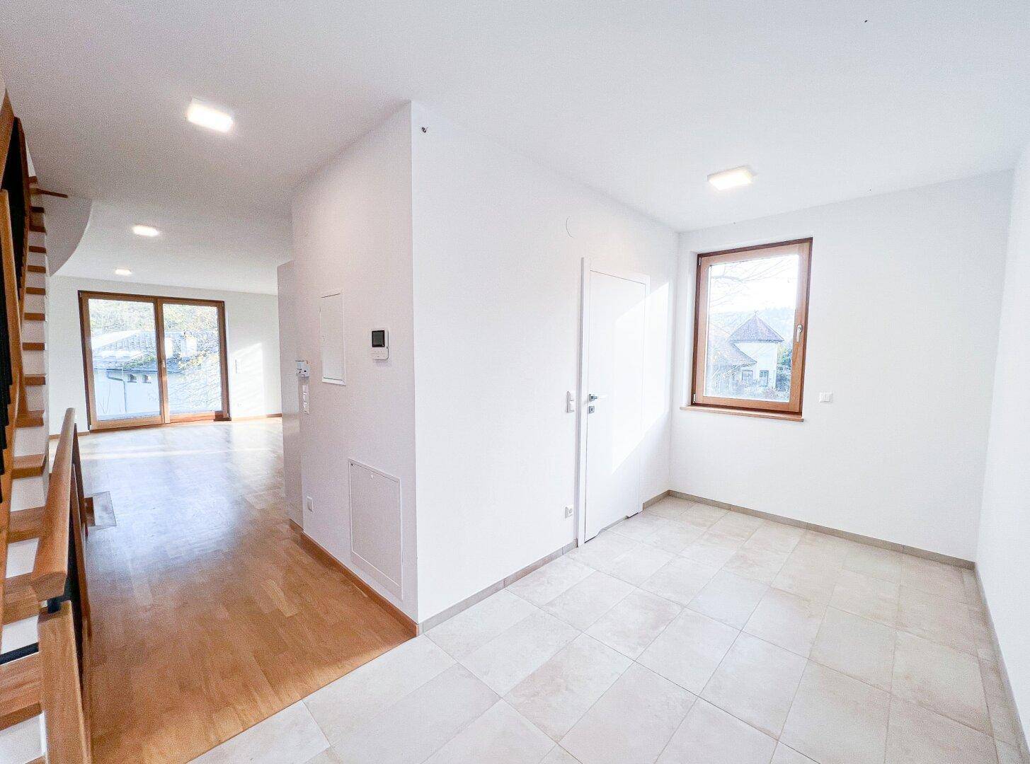 Heller Eingangsbereich mit Fliesenboden und Holztreppe, führt in den offenen Wohnbereich.