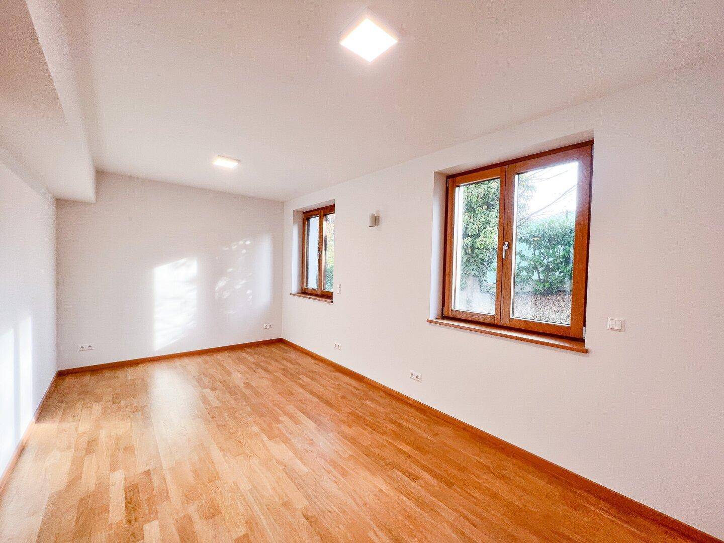 Helles Zimmer mit Parkettboden und großen Fenstern, bietet vielseitige Nutzungsmöglichkeiten.