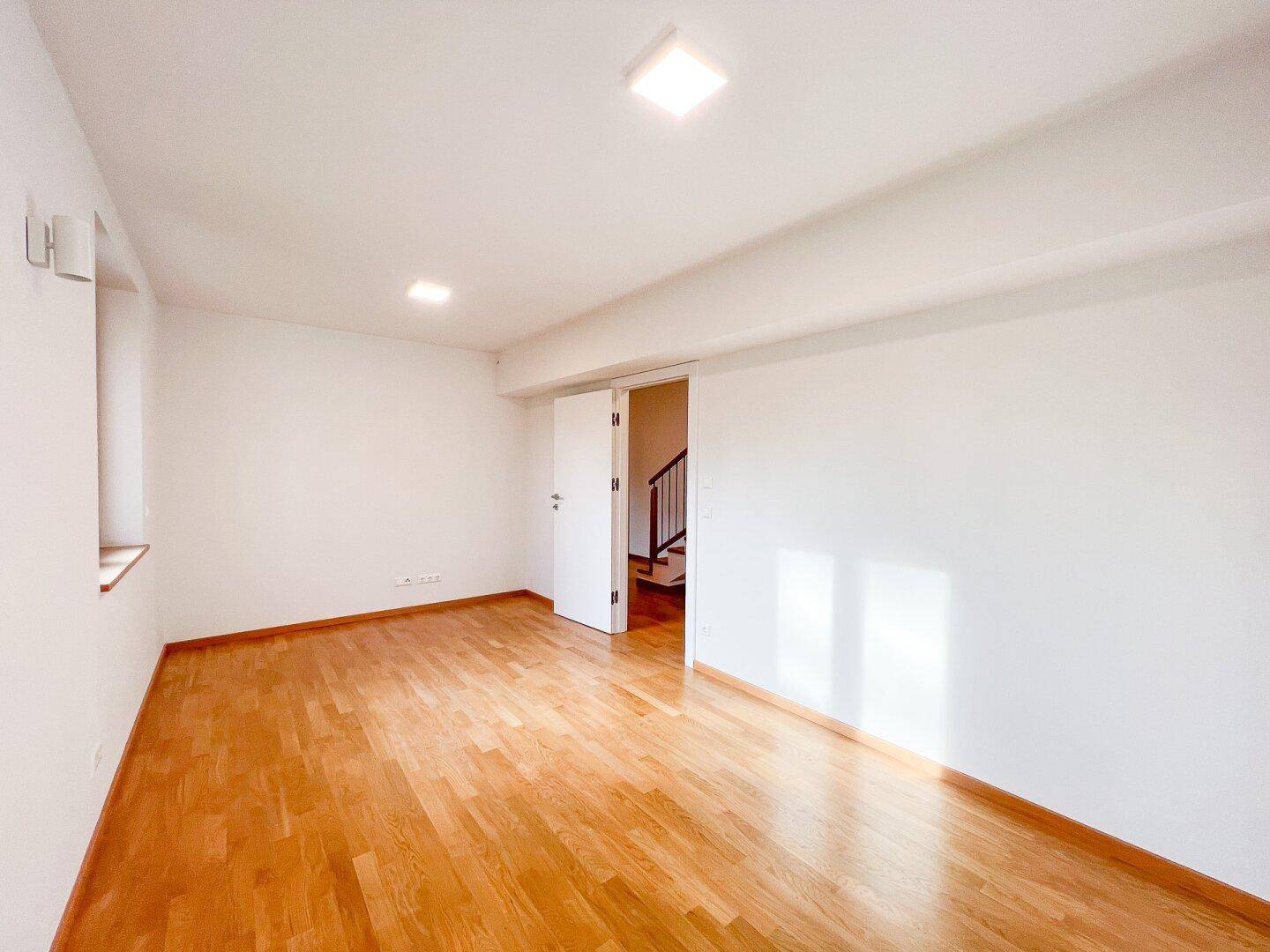 Geräumiges Zimmer mit Holzboden und Zugang zum Flur, ideal als Schlaf- oder Arbeitszimmer.
