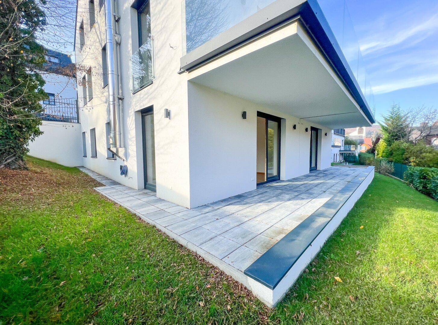 Moderne Gebäudeseite mit großer Terrasse und gepflegtem Rasen, bietet viel Platz im Freien.