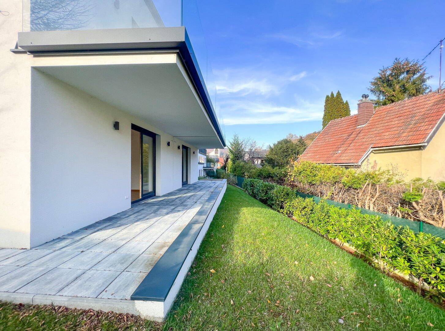 Geräumige Terrasse mit Steinplatten und angrenzendem Rasenbereich, umgeben von Hecken.