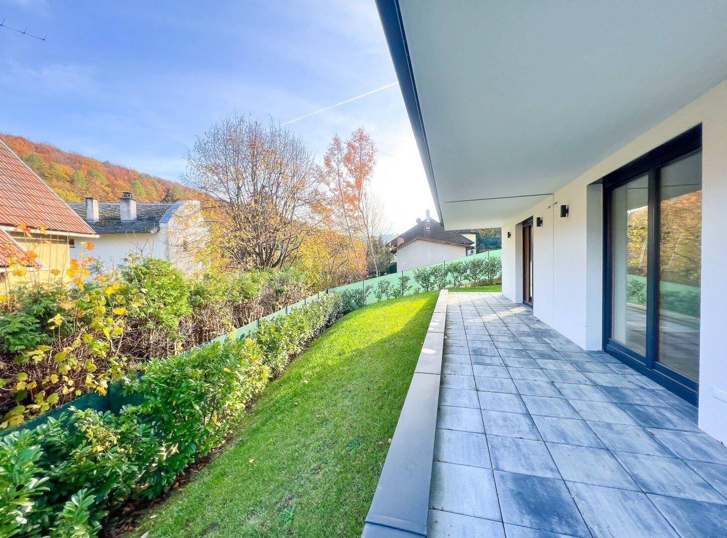 Lange Terrasse mit Steinplatten und angrenzendem Rasen, bietet einen sonnigen Außenbereich.