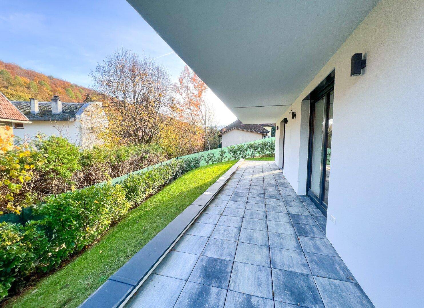Sonniger Terrassenbereich mit Steinplatten und gepflegtem Rasen, ideal zum Entspannen im Freien.