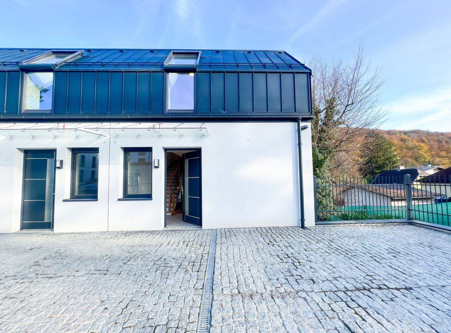 Eingangsbereich des modernen Reihenhauses mit gepflastertem Vorplatz und dunkler Eingangstür.