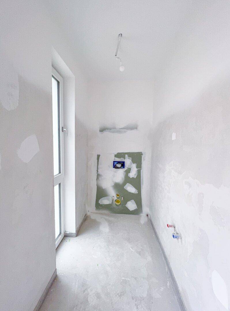 Schmaler Raum im Rohbau mit Fenster und Sanitärinstallationen, ideal für ein Gäste-WC.