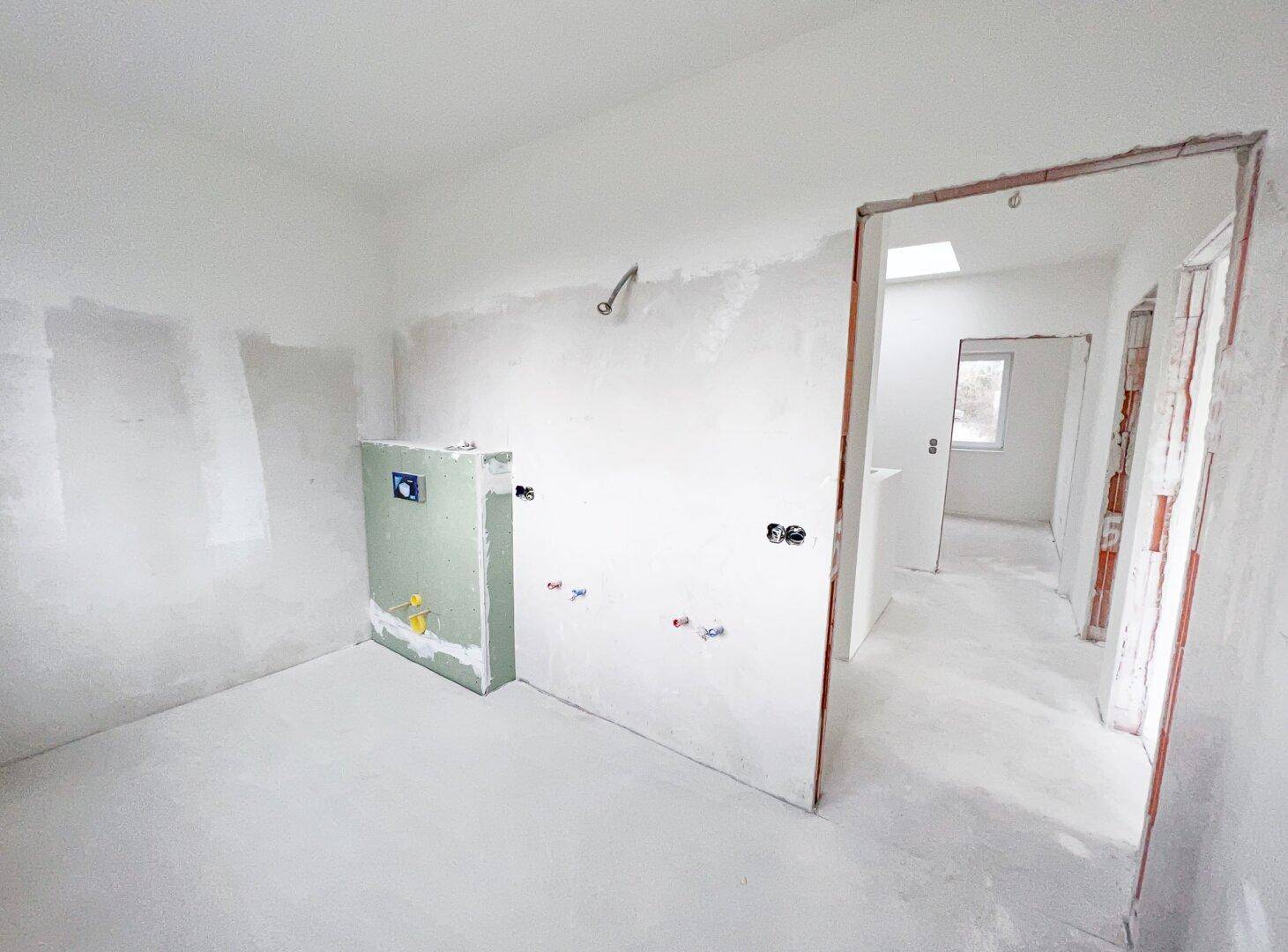 Badezimmer im Rohbau mit sichtbaren Installationen und Dachfenster, bereit für den Ausbau.
