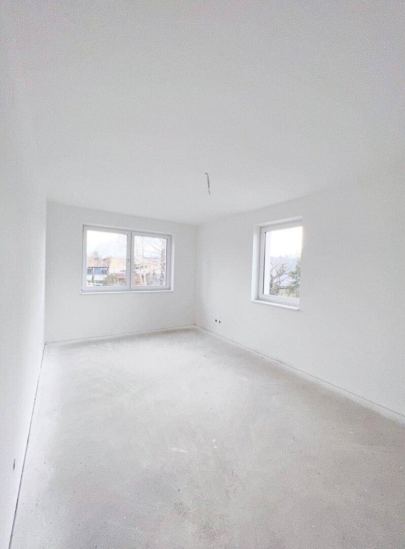 Helles, leeres Zimmer mit zwei Fenstern und sauberem Estrichboden, ideal für Schlaf- oder Arbeitszimmer.