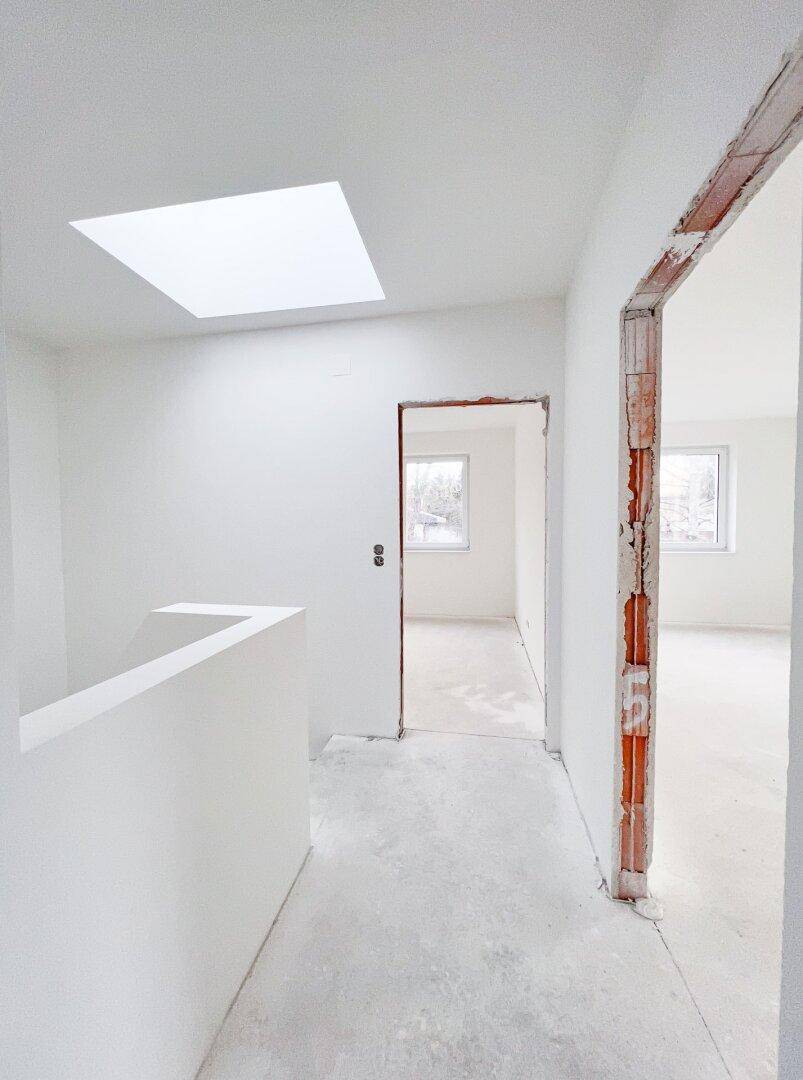 Heller Flur im Rohbau mit Dachfenster und Zugang zu weiteren Räumen, viel Tageslicht.