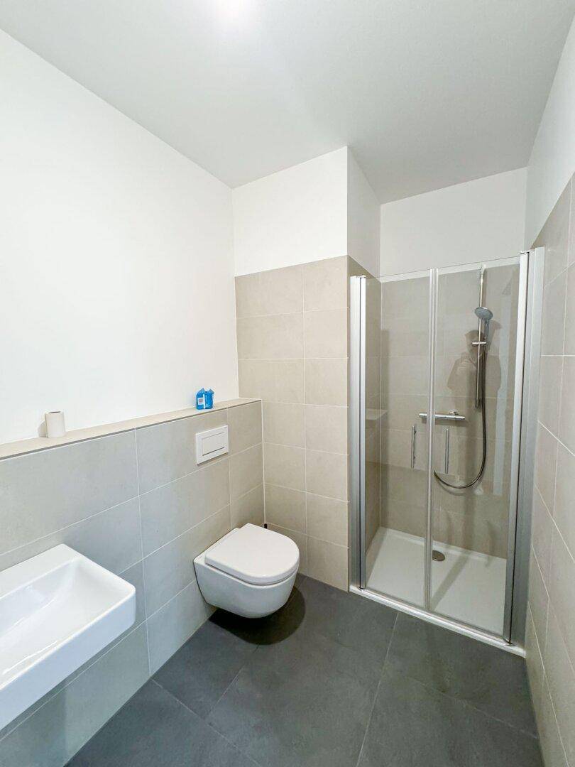 Modernes Badezimmer mit Duschkabine, wandhängendem WC und hellen Fliesen an Wänden und Boden.