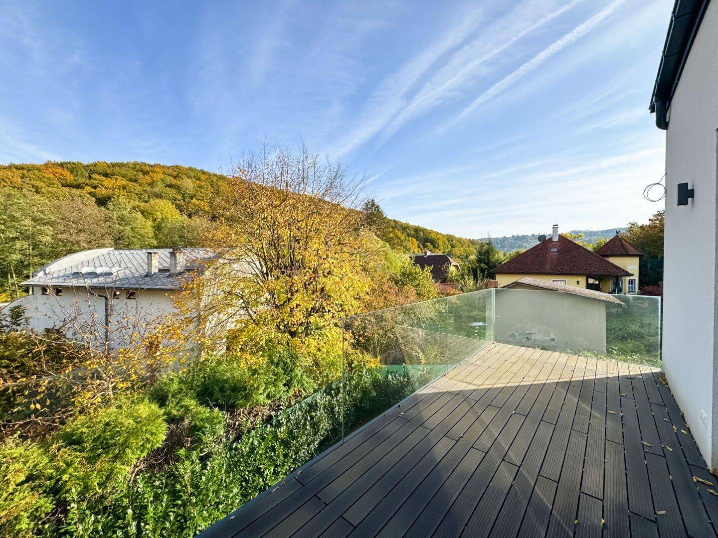 Großer Balkon mit Holzbelag und Glasgeländer, bietet weite Aussicht auf die bewaldete Umgebung.