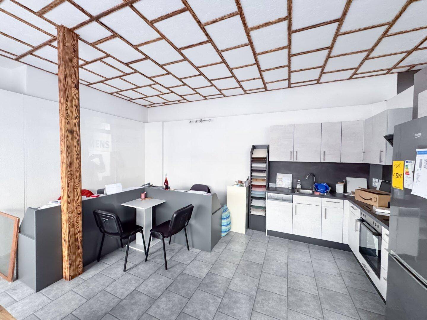 Funktionale Küche mit Einbaugeräten und einem kleinen Essbereich, ergänzt durch eine Holzsäule und Deckenverkleidung.