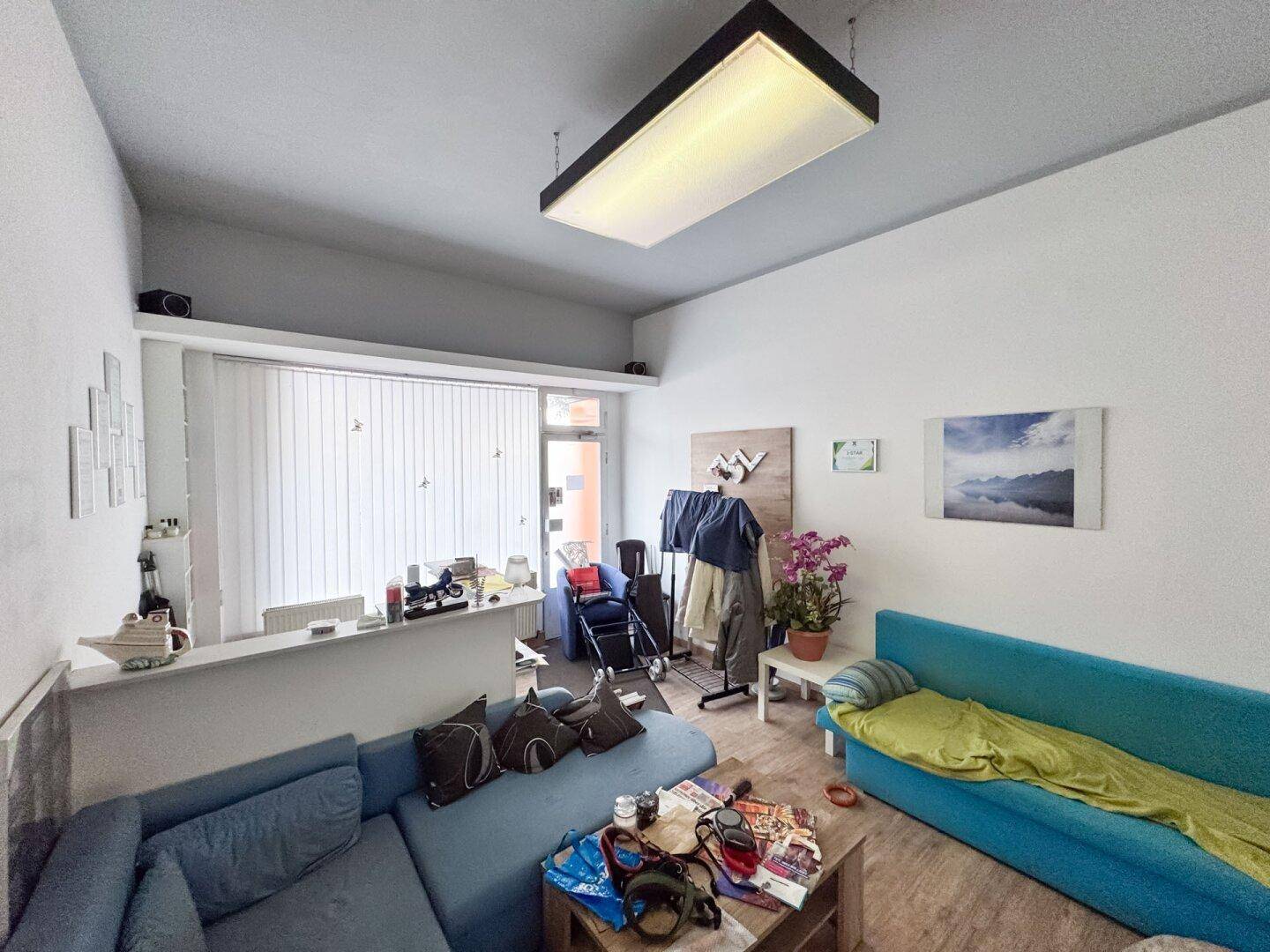 Heller Wohnbereich mit großem Fenster, Jalousien, einem bequemen Ecksofa und Laminatboden.