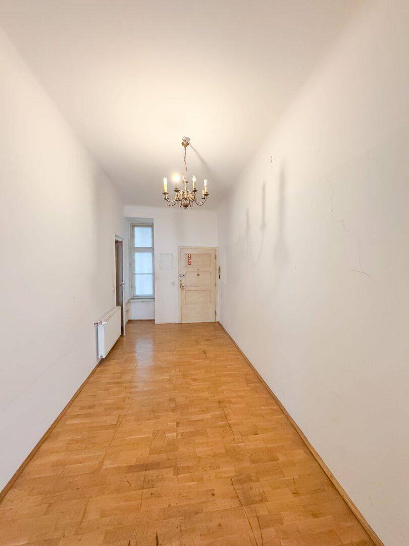 Geräumiger Flur mit Fischgrätparkett und einem klassischen Kronleuchter, der den Eingangsbereich beleuchtet.