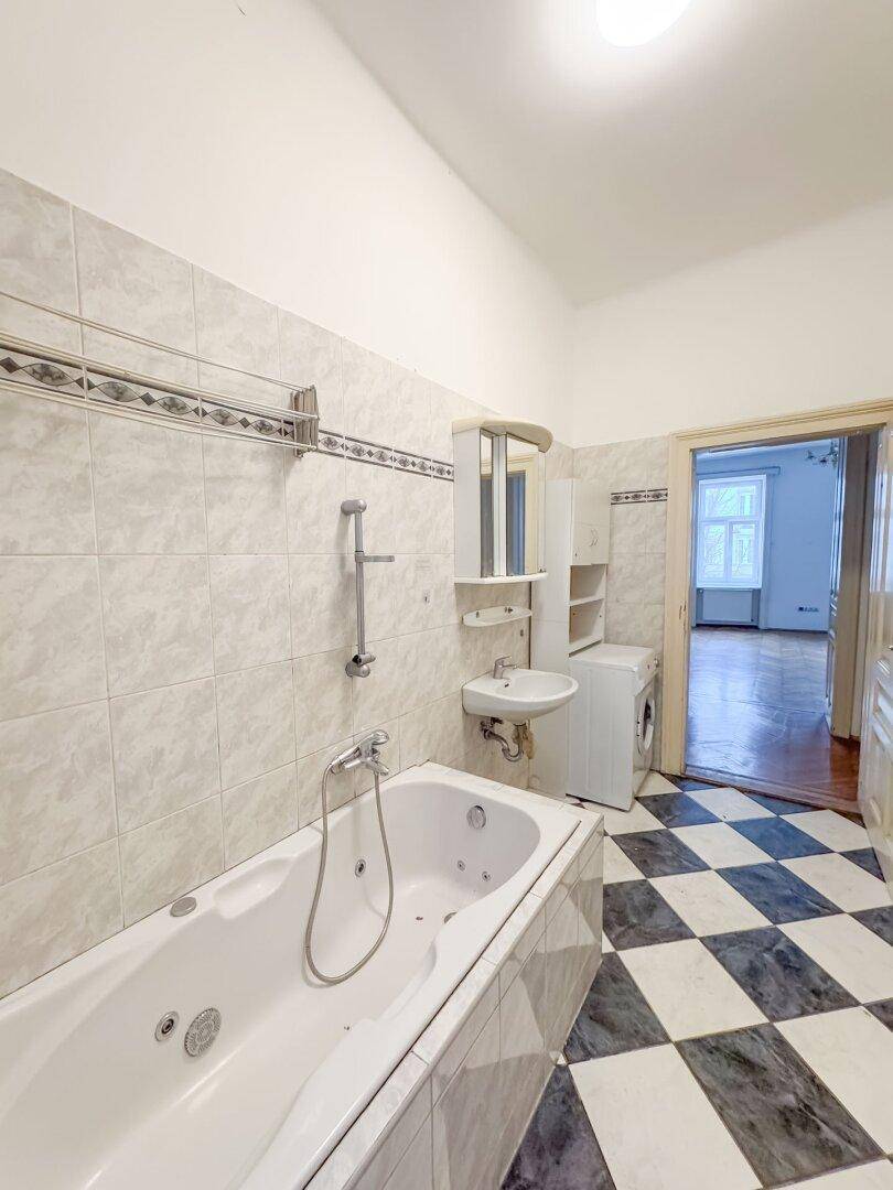 Badezimmer mit Badewanne, Waschbecken, Spiegelschrank und Blick in den angrenzenden Raum.