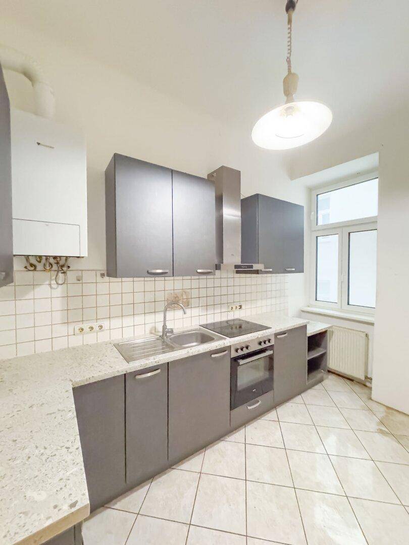 Helle Küche mit grauen Unterschränken, Granitarbeitsplatte, Fliesenboden und Fenster.