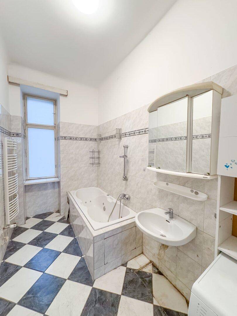 Badezimmer mit Schachbrettmuster-Fliesen, Badewanne mit Whirlpoolfunktion und Fenster.