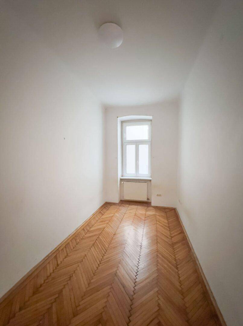 Schmaler Raum mit Fischgrätparkett und einem Fenster, ideal als Schlaf- oder Arbeitszimmer.