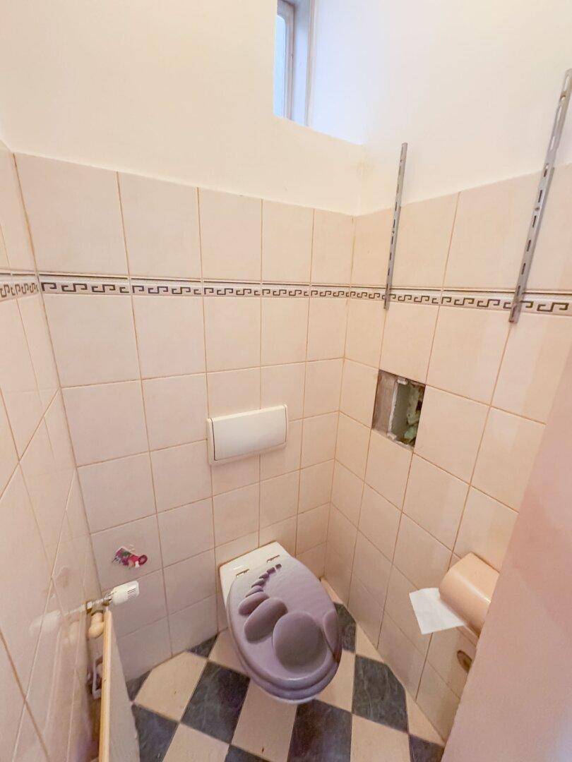 Kleines WC mit Fliesenboden und Wand-WC, ausgestattet mit einem Fenster für Tageslicht.