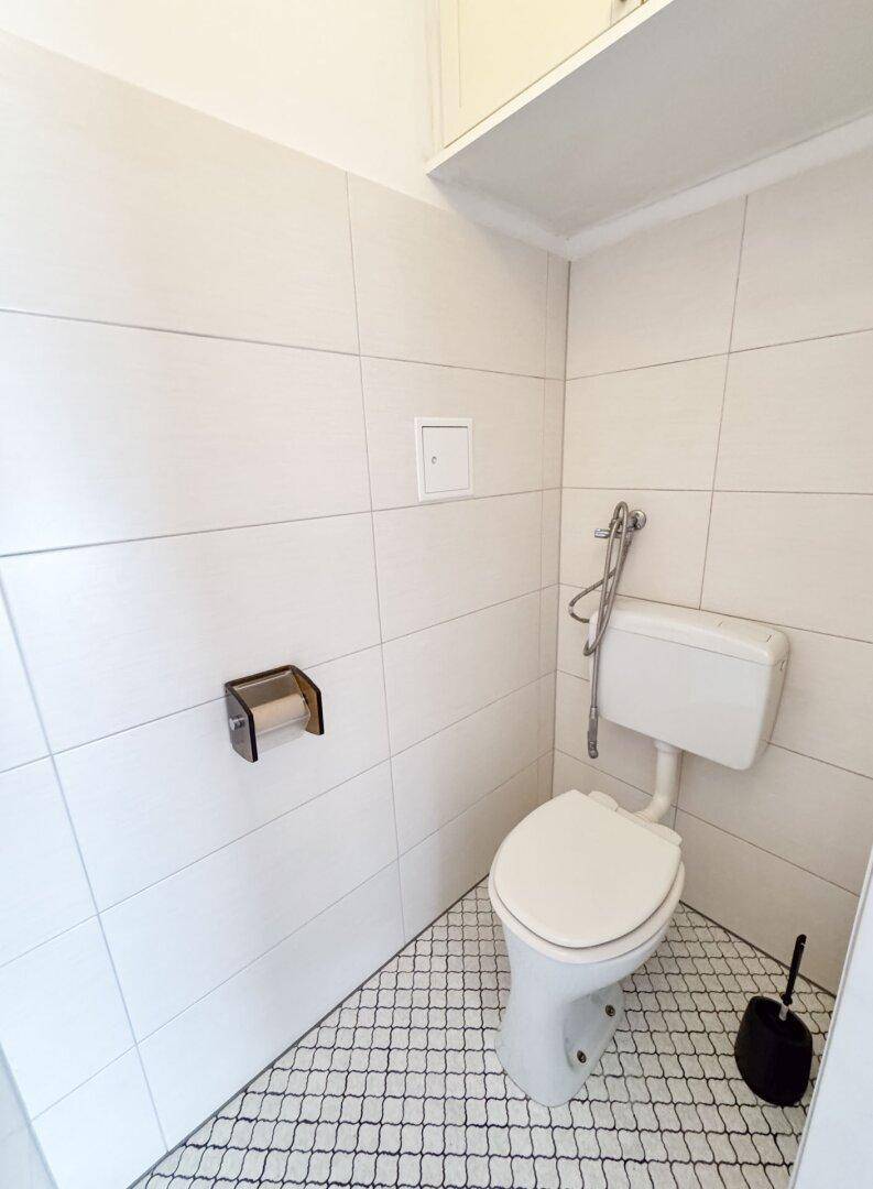 Separate Toilette mit weißen Fliesen und einem funktionalen WC, ideal für Gäste.