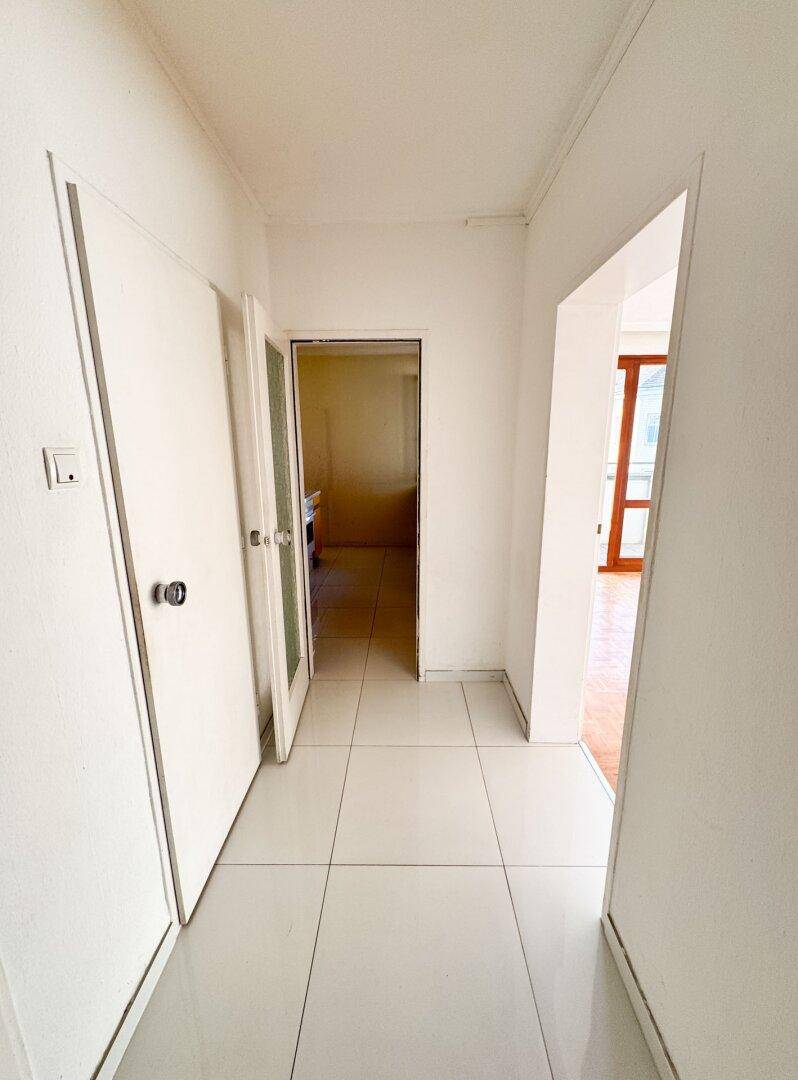 Heller Flur mit Fliesenboden, der zu weiteren Räumen und einem Balkon führt.
