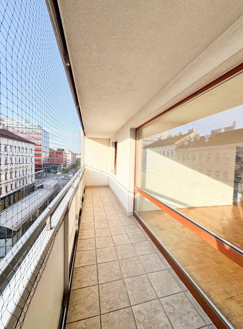 Langer Balkon mit Fliesenboden und Schutznetz, bietet einen weiten Blick über die Stadt.
