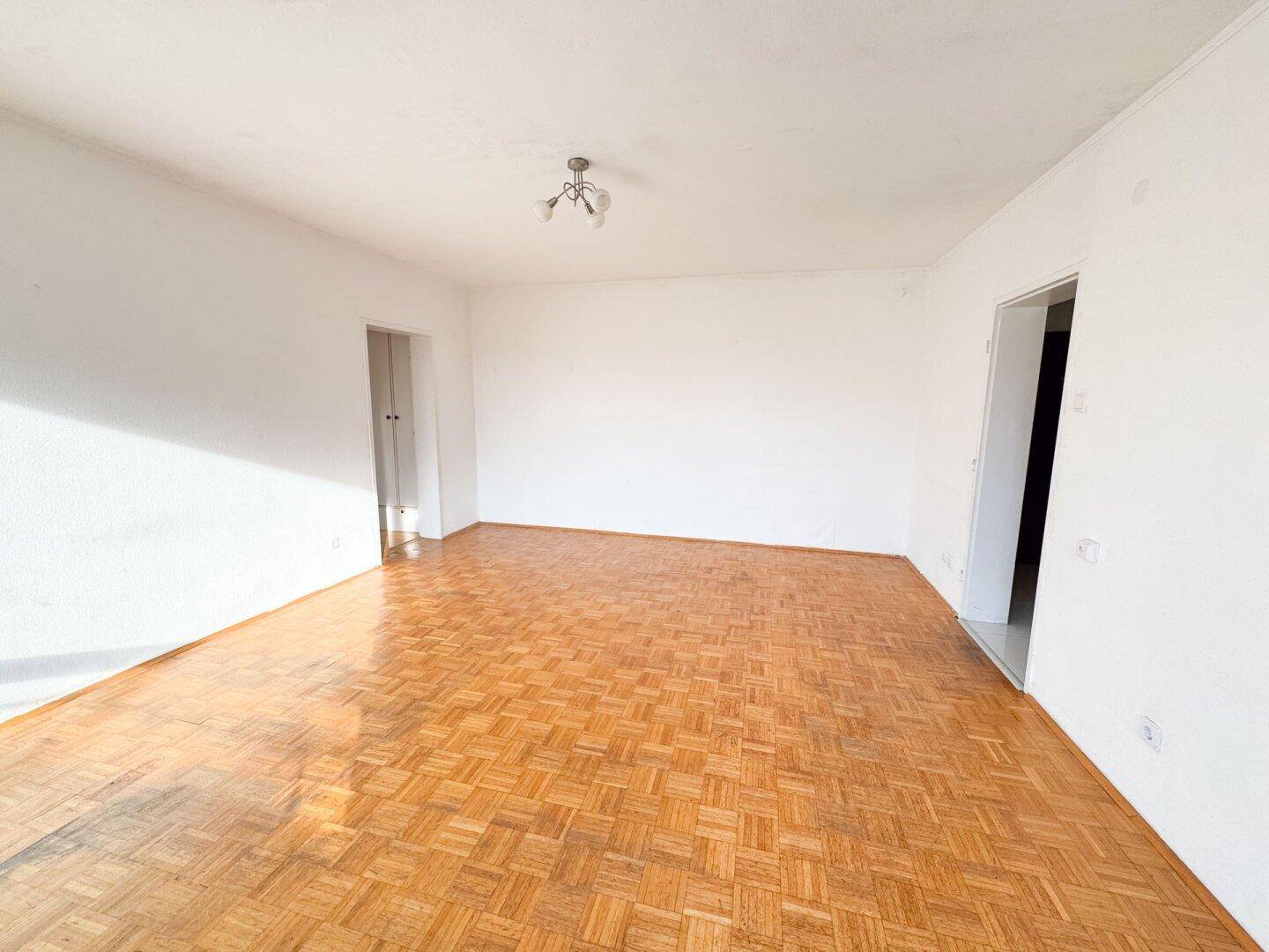 Leerer Raum mit Parkettboden und weißen Wänden, bereit zur individuellen Gestaltung.