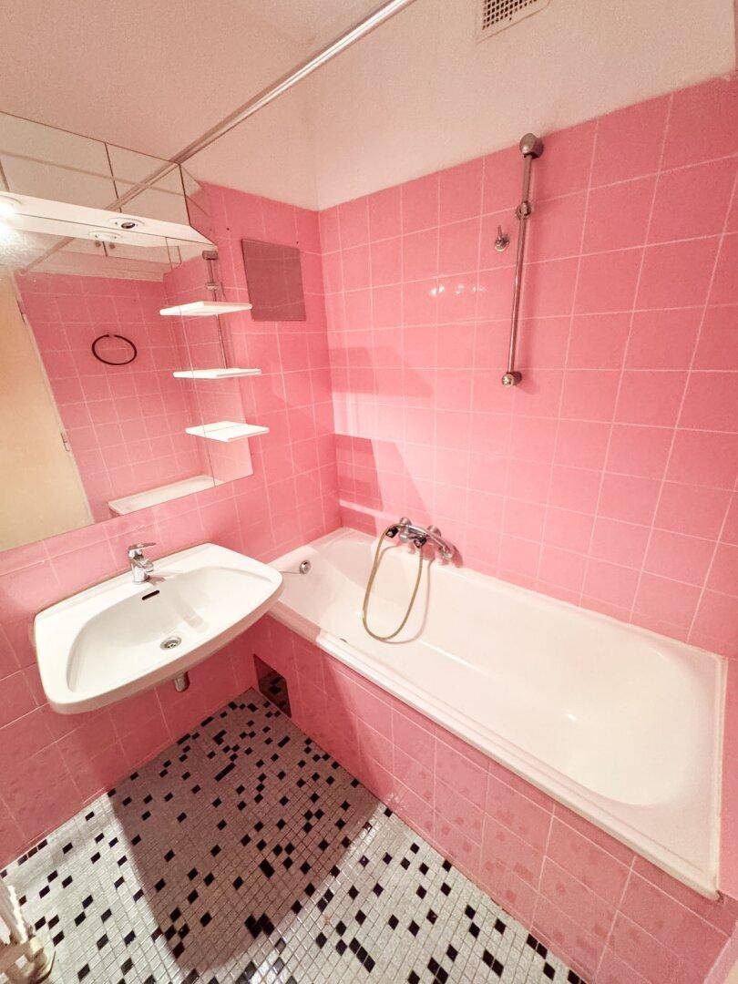Badezimmer im 80er-Jahre-Stil mit rosa Fliesen, Badewanne und Waschbecken.