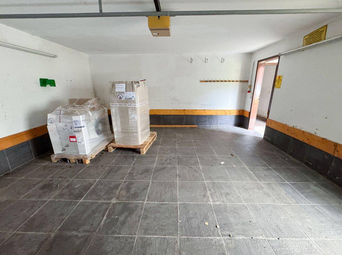 Geräumige Garage mit Fliesenboden und Lagerkartons, bietet Platz für Fahrzeuge und Stauraum.