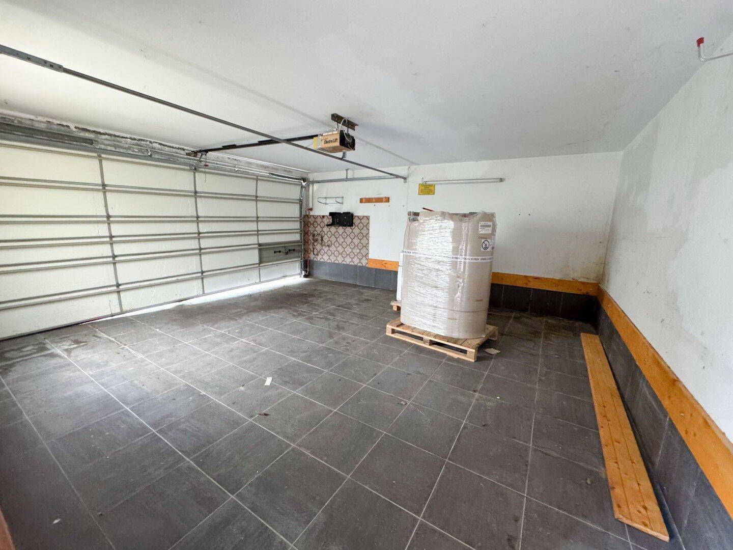 Leere Garage mit Rolltor und Fliesenboden, ideal für Fahrzeuge oder als Werkstatt.