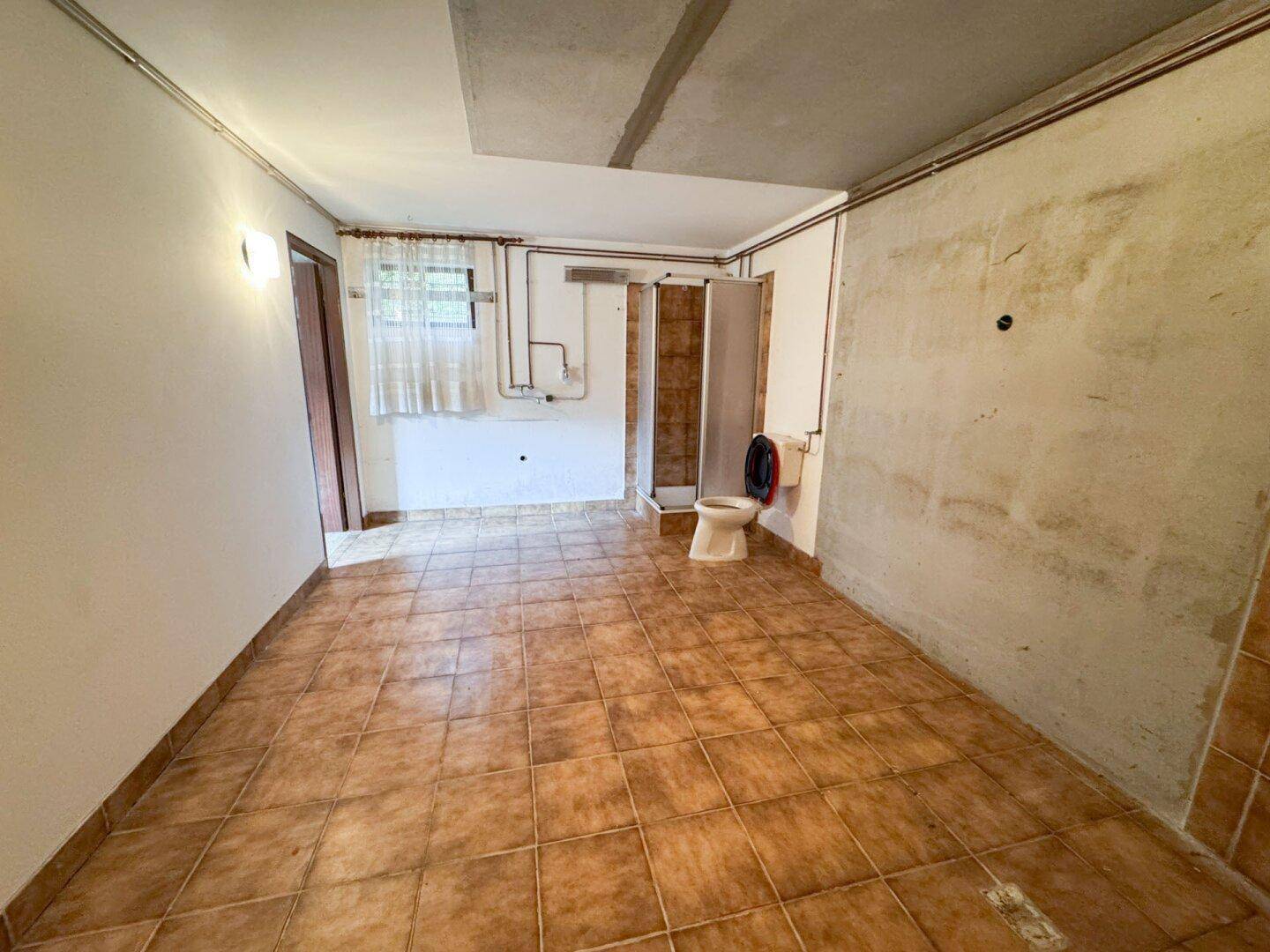 Kellerraum mit Fliesenboden und einfacher Toilette, bietet zusätzlichen Nutzraum.