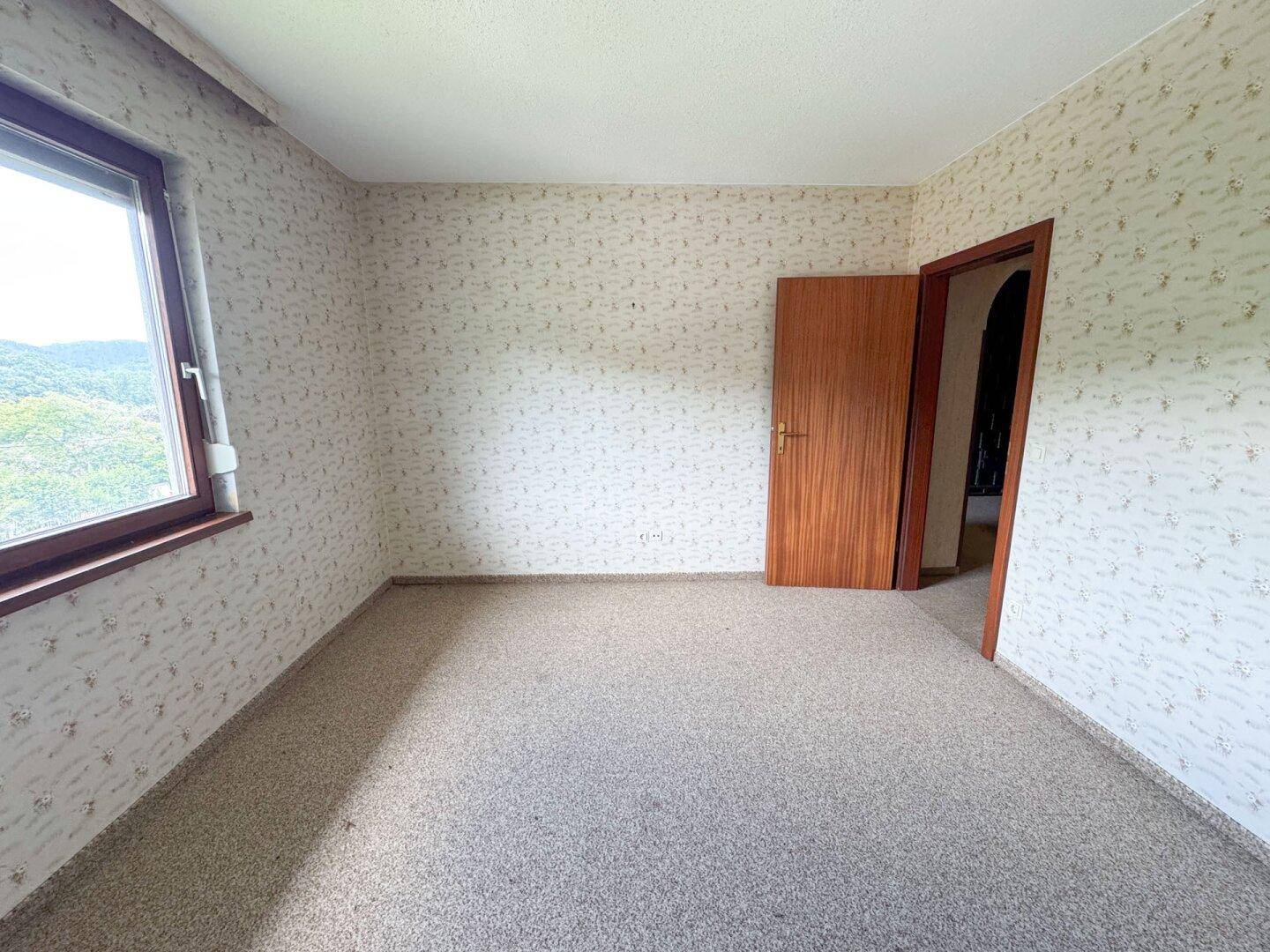 Schlafzimmer mit gemusterter Tapete und Teppichboden, bietet einen Blick ins Grüne.