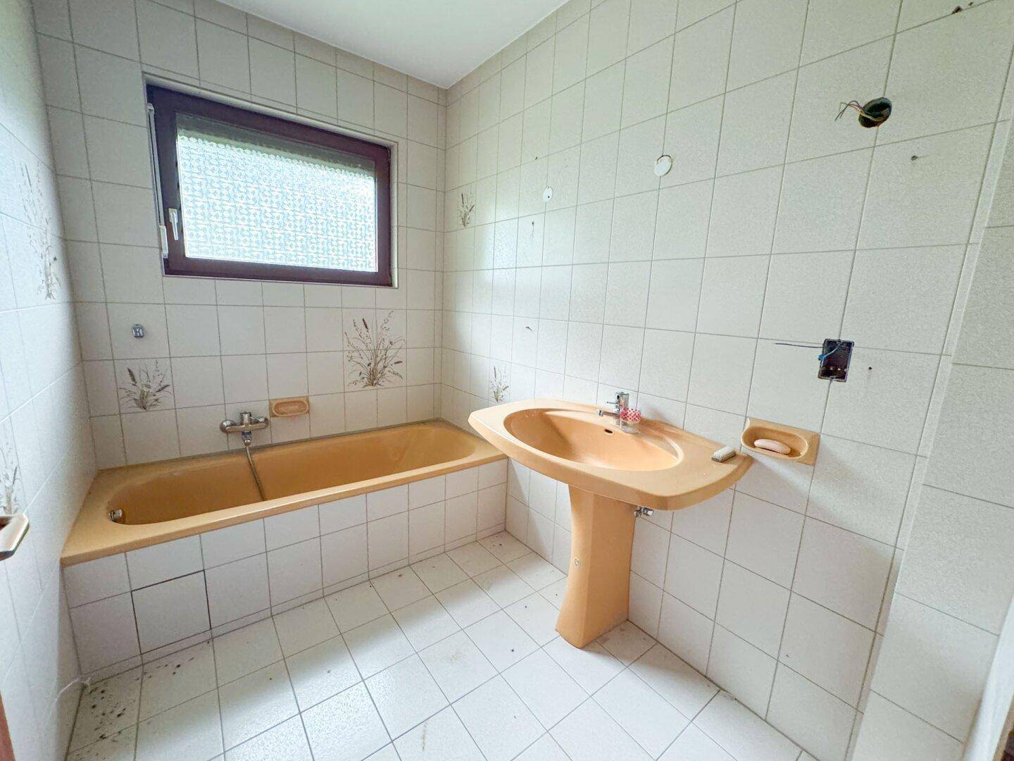 Badezimmer im Stil der 80er Jahre mit gelber Badewanne und Waschbecken, gefliest.