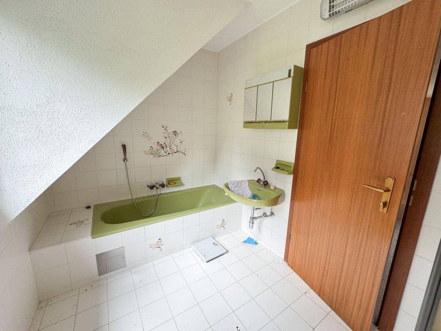 Badezimmer im Stil der 80er Jahre mit grüner Badewanne und Dachschräge, gefliest.