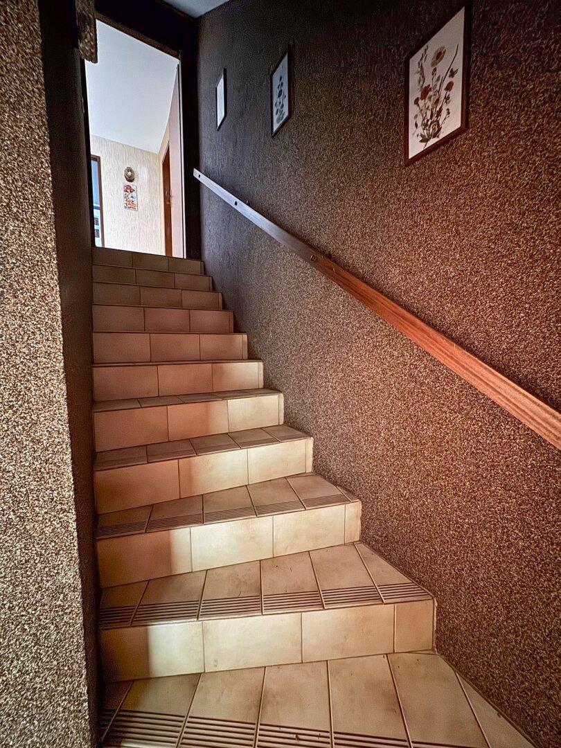Geflieste Treppe mit Holzgeländer und strukturierter Wandverkleidung, führt nach oben.