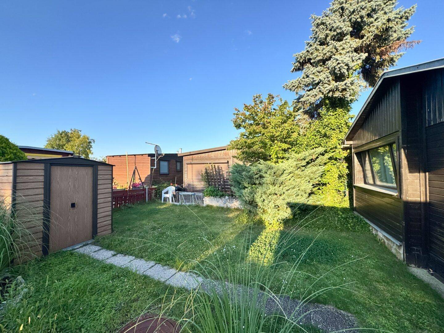 Gepflegter Gartenbereich mit Rasenfläche, Gartenhaus und Blick auf weitere Bungalows.