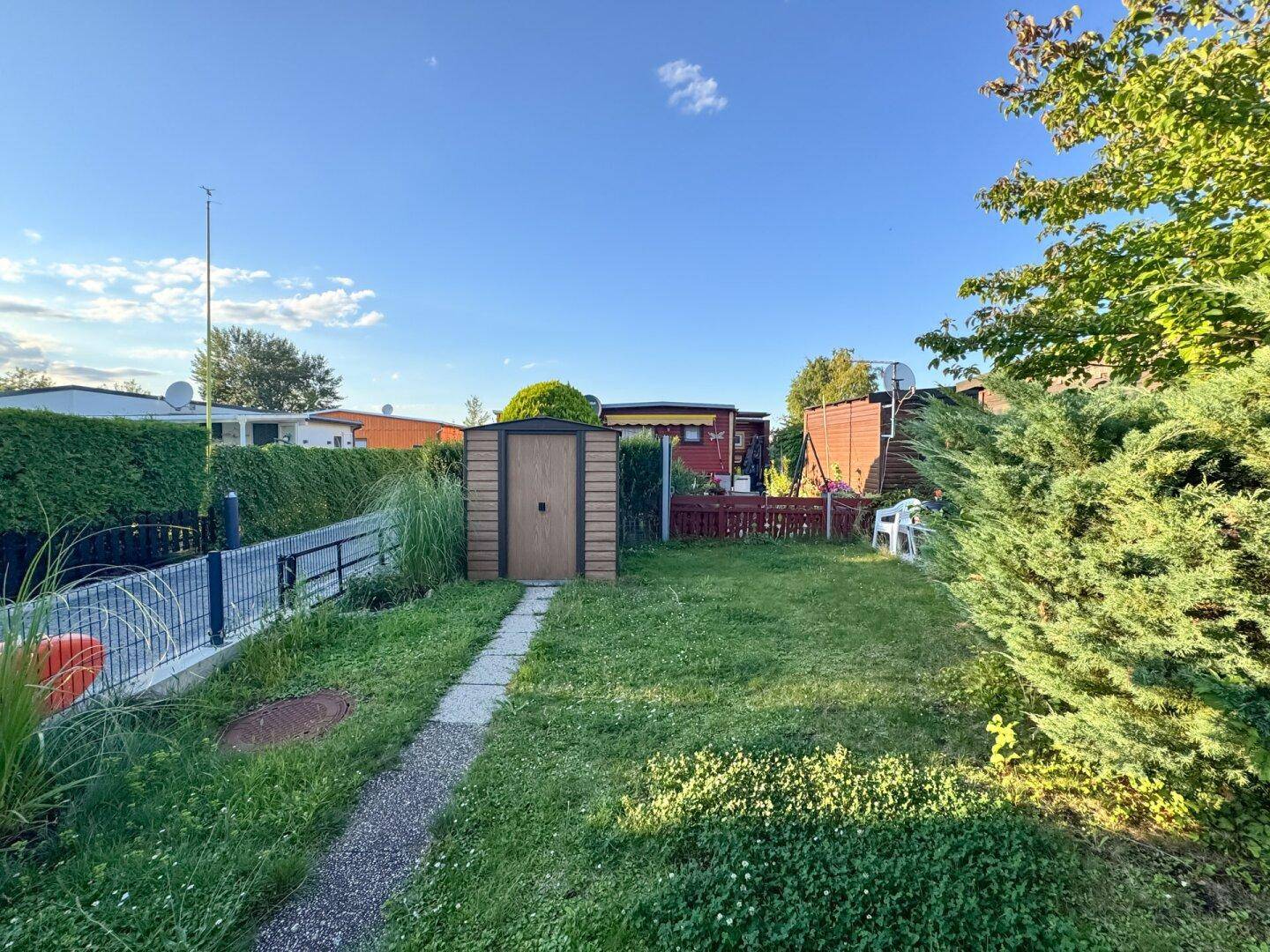 Weitläufiger Gartenbereich mit Rasen, Hecke und einem praktischen Gartenhaus.