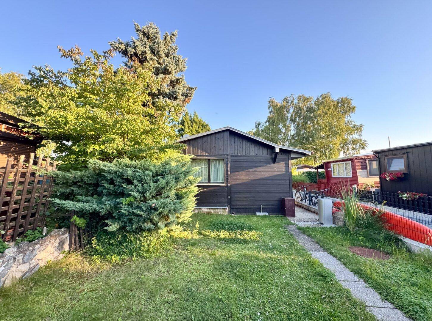 Seitlicher Blick auf den Holzbungalow mit angrenzendem Garten und gepflastertem Weg.