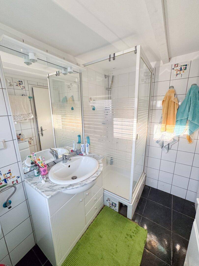 Helles Badezimmer mit Dusche, Waschbecken und weißen Fliesen mit bunten Akzenten.