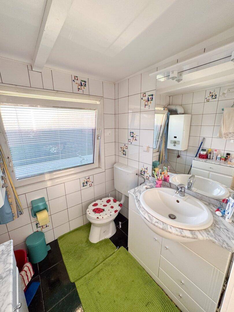 Badezimmer mit WC, Waschbecken, Fenster und weißen Fliesen mit farbigen Mustern.