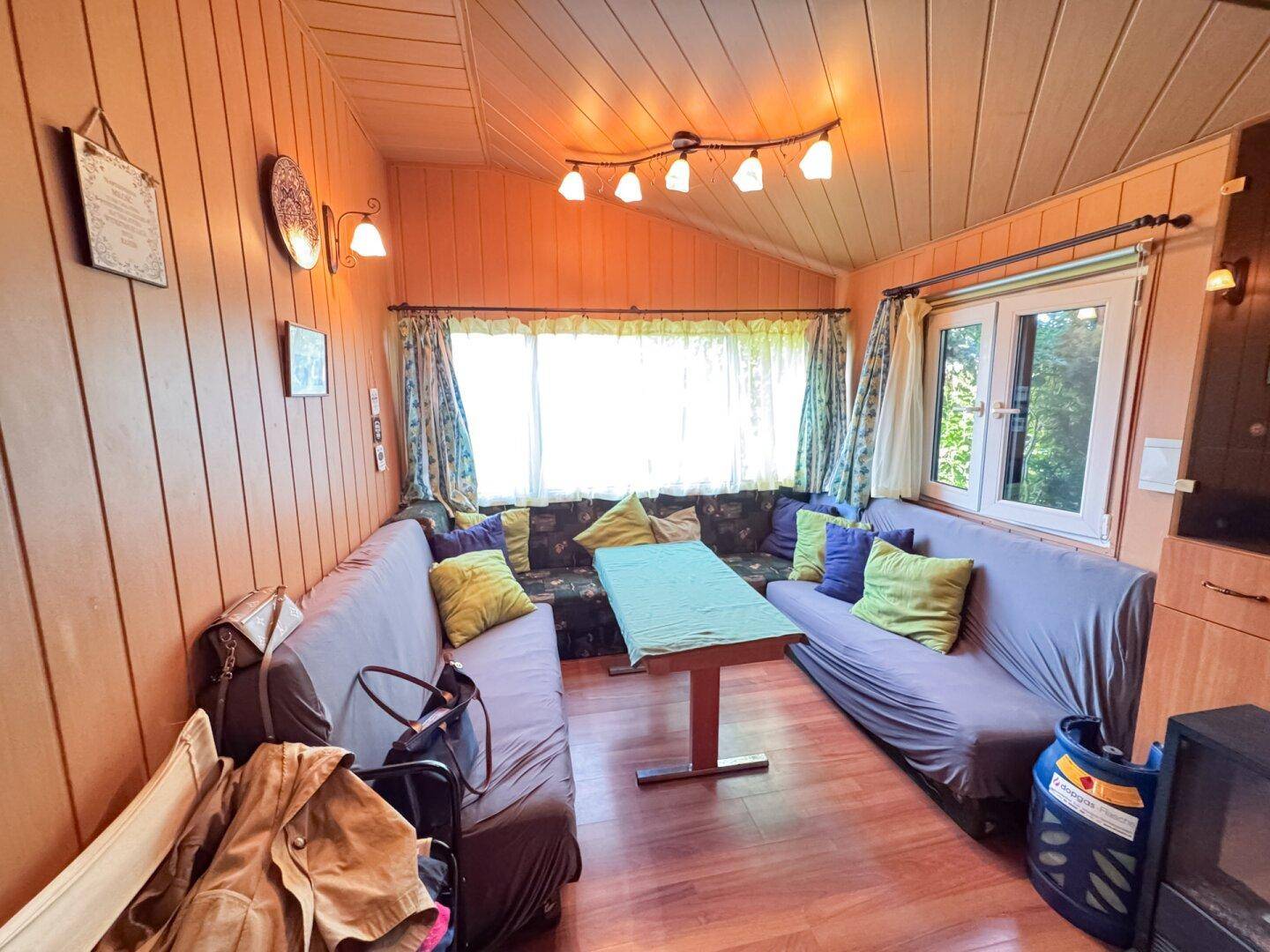 Gemütliches Wohnzimmer mit Holzverkleidung, Ecksofas und einem kleinen Esstisch.